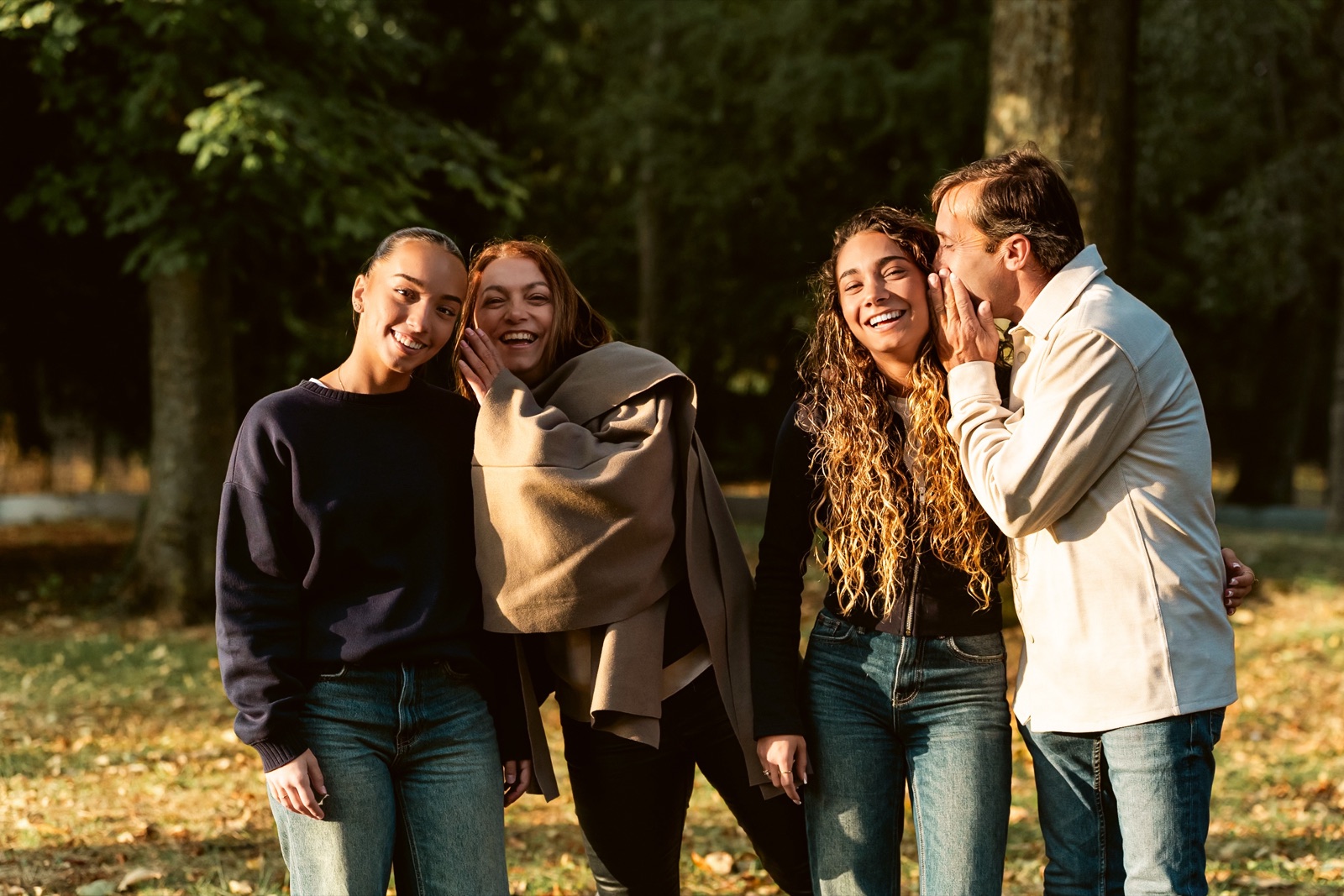 Une famille qui rit dans un parc d'automne, un homme chuchotant à l'oreille d'une jeune femme.